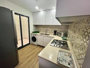 A compact kitchen with a washing machine, a sink, a stove, and a microwave.