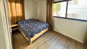 Ein kleines Zimmer mit einem Einzelbett, einem Fenster, Holzboden und einem Bett mit einem gemusterten Überwurf.