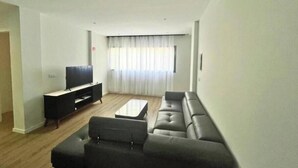 Ein Wohnzimmer mit einer Sofagarnitur, einem Couchtisch und einem Fernseher auf einem Schrank.