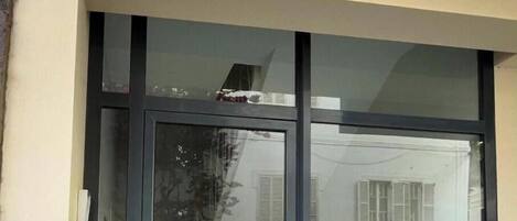 Une entrée d’immeuble avec une porte en verre, une plaque portant le numéro « 11 », et le reflet d’une maison avec des volets.