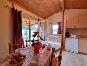 Ein gemütliches Zimmer mit Esstisch, Stühlen, einer Küchenzeile und Blick ins Freie.