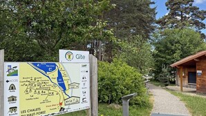 A wooden cabin with a sloped roof, a gravel path leading to it, and a signboard with a map and text.