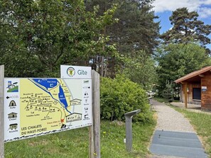 Eine Holzhütte mit geneigtem Dach, ein Kiesweg, der dorthin führt, und ein Schild mit einer Karte und Text.