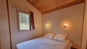 A bedroom with a wooden ceiling, a window with curtains, two bedside lamps, and a bed with white bedding.