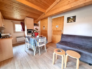 A cozy room with a wooden ceiling, a dining table with chairs, a sofa, and a small table with a magazine. - PMR Chalet, pets welcome - 4 guests (Usson-en-Forez)