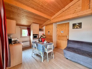 Ein gemütliches Blockhaushaus-Interieur mit Esstisch, Stühlen, einer Küchenzeile und einer Couch.