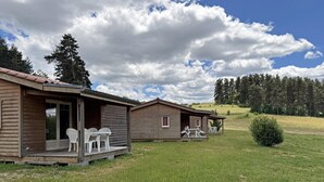 Dos cabañas de madera con mobiliario exterior, rodeadas de un campo cubierto de césped y árboles.