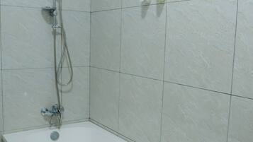 A bathroom with a bathtub, a showerhead, and a towel on the edge.