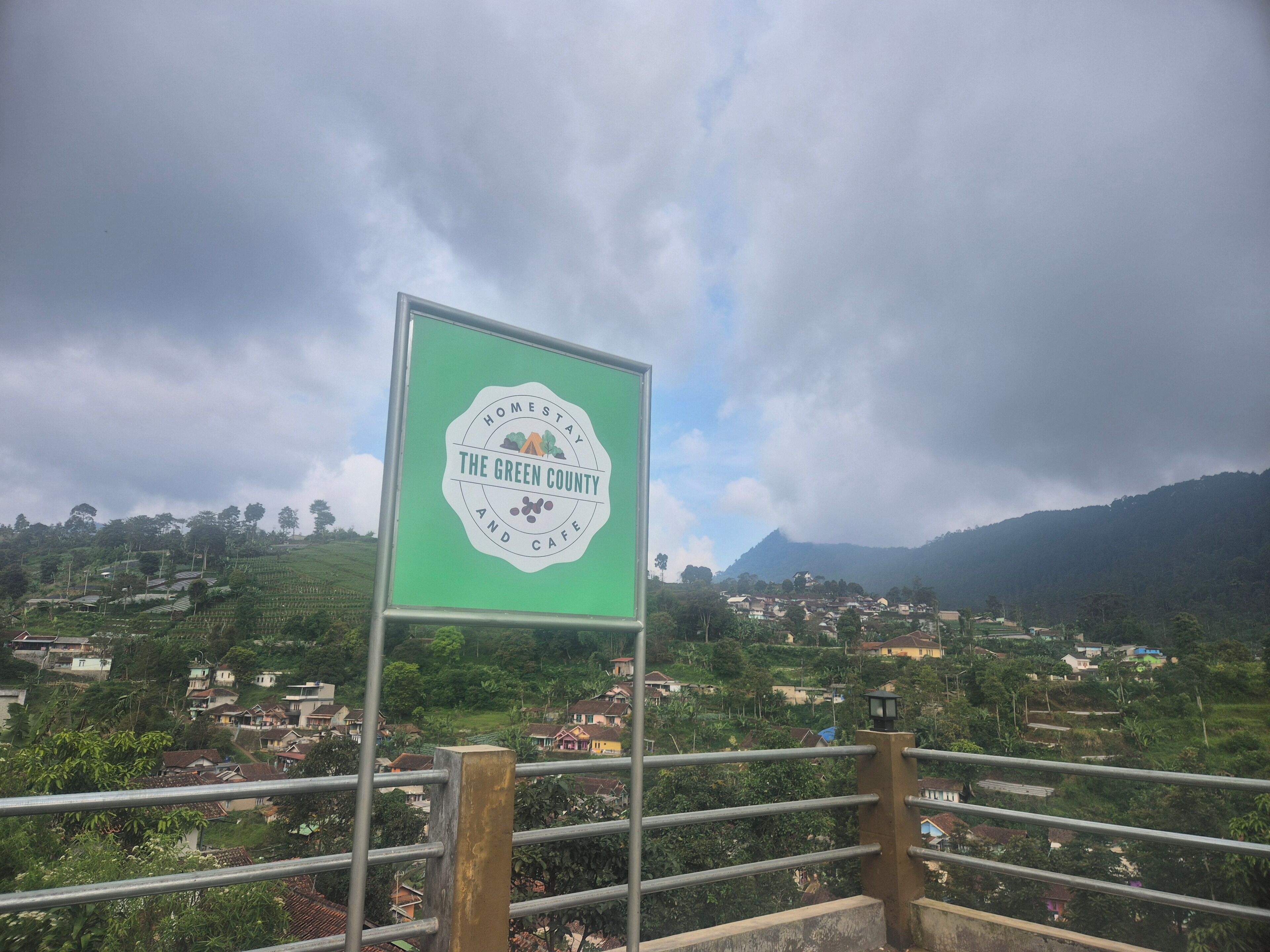 Un cartel que dice 'The Green County and Cafe' con vistas a un paisaje montañoso y casas al fondo.