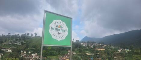 Un cartel que dice 'The Green County and Cafe' con vistas a un paisaje montañoso y casas al fondo.