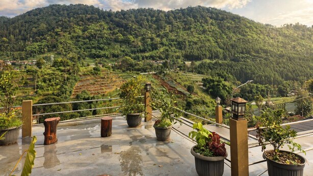 Una terraza en la azotea con plantas en macetas, barandilla y vistas a un valle verde exuberante con campos escalonados.