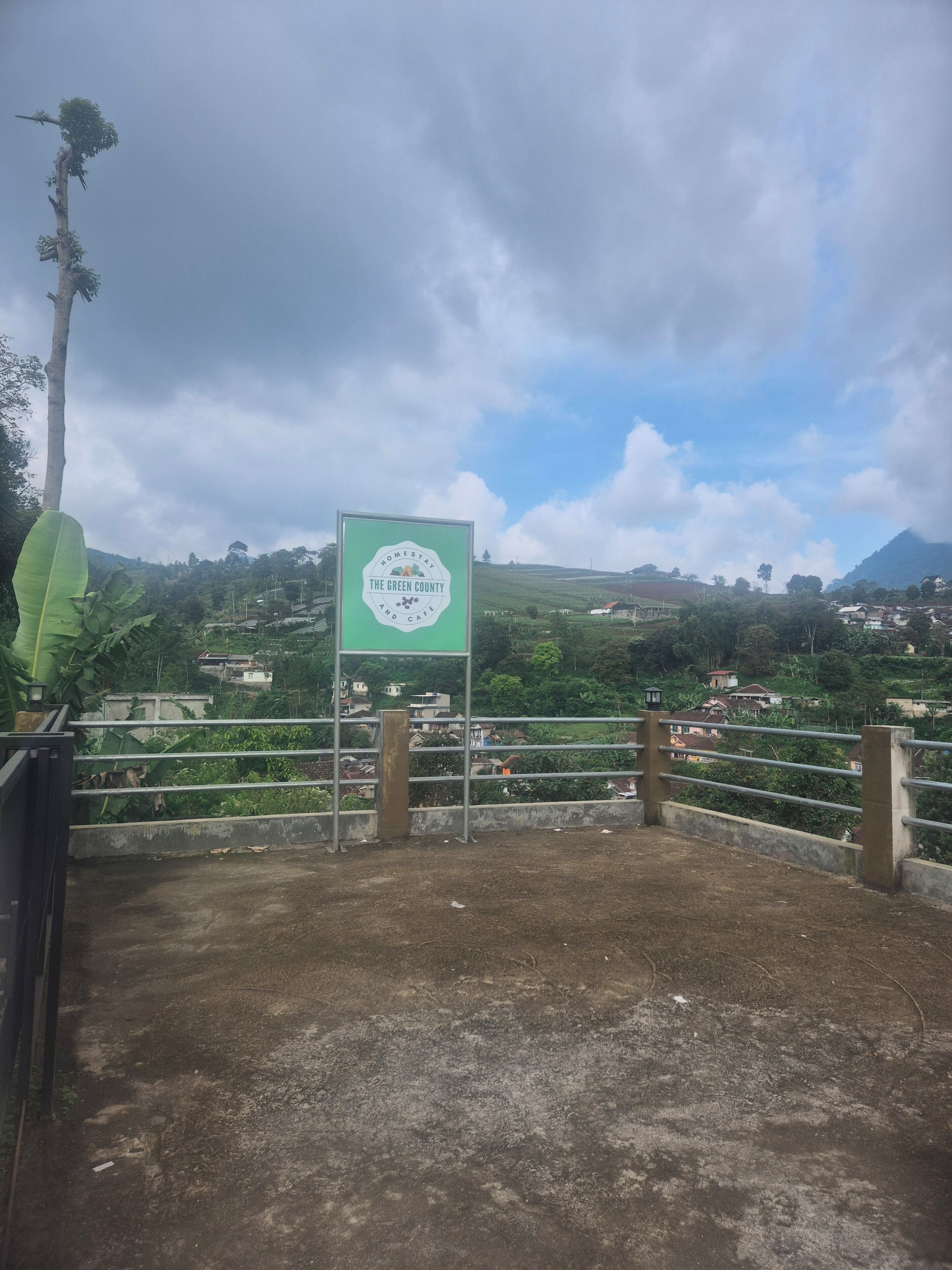 Un cartel que dice 'The Green County', con vistas a un paisaje montañoso y casas al fondo.