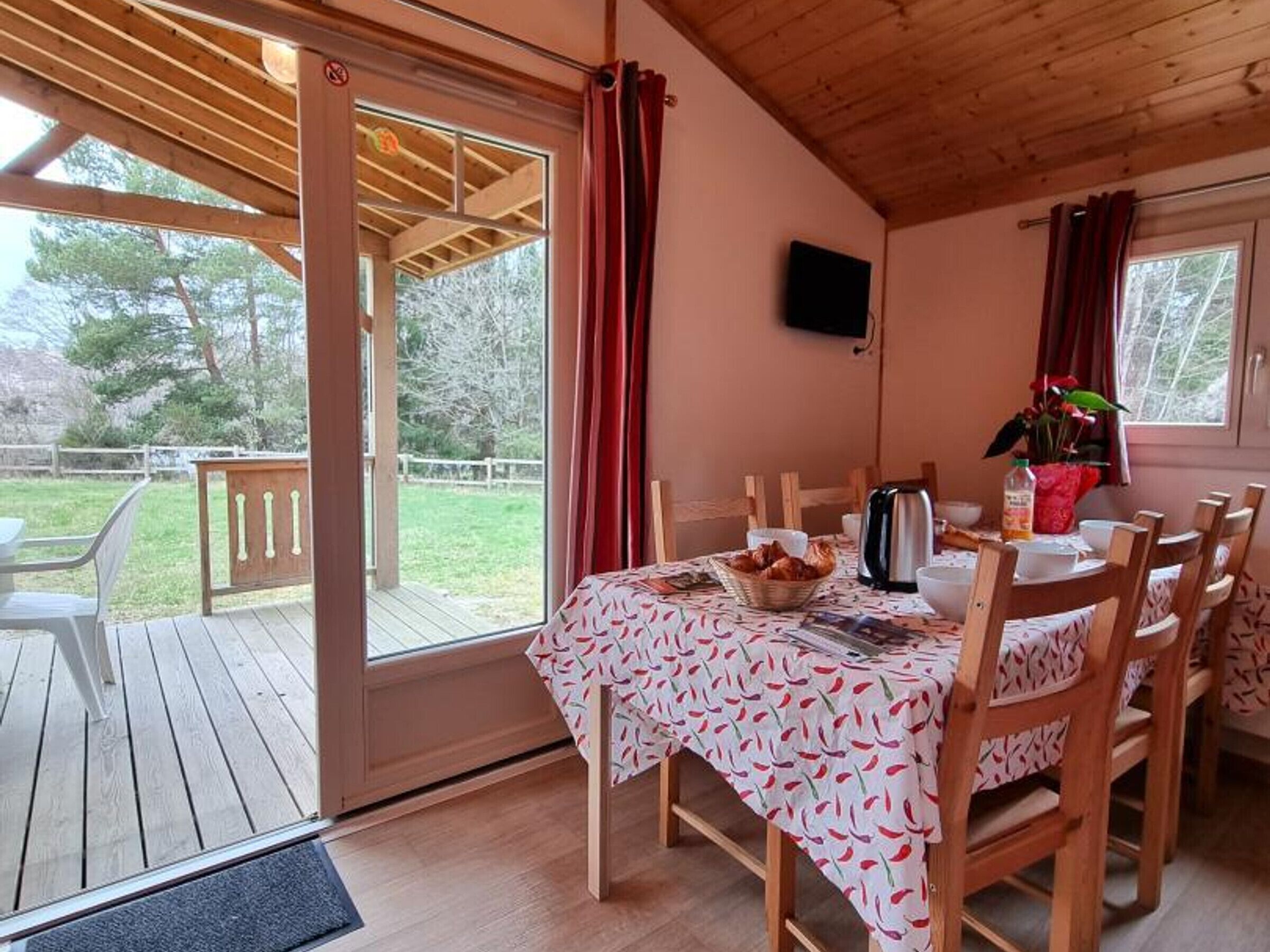 A dining area with a table set for four, a wooden deck outside, and a television mounted on the wall.