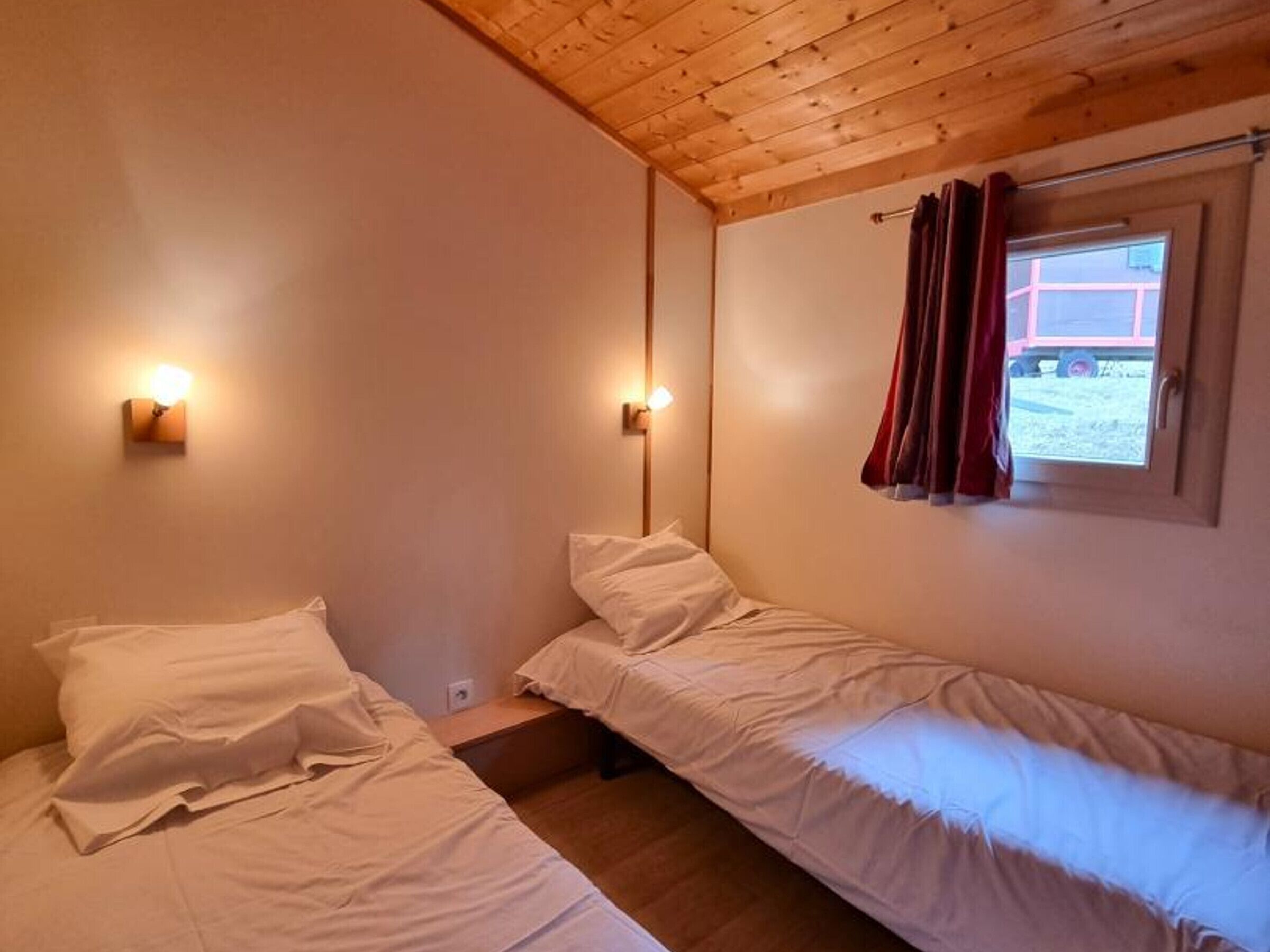 A room with two single beds, wooden ceiling, and a window with curtains.