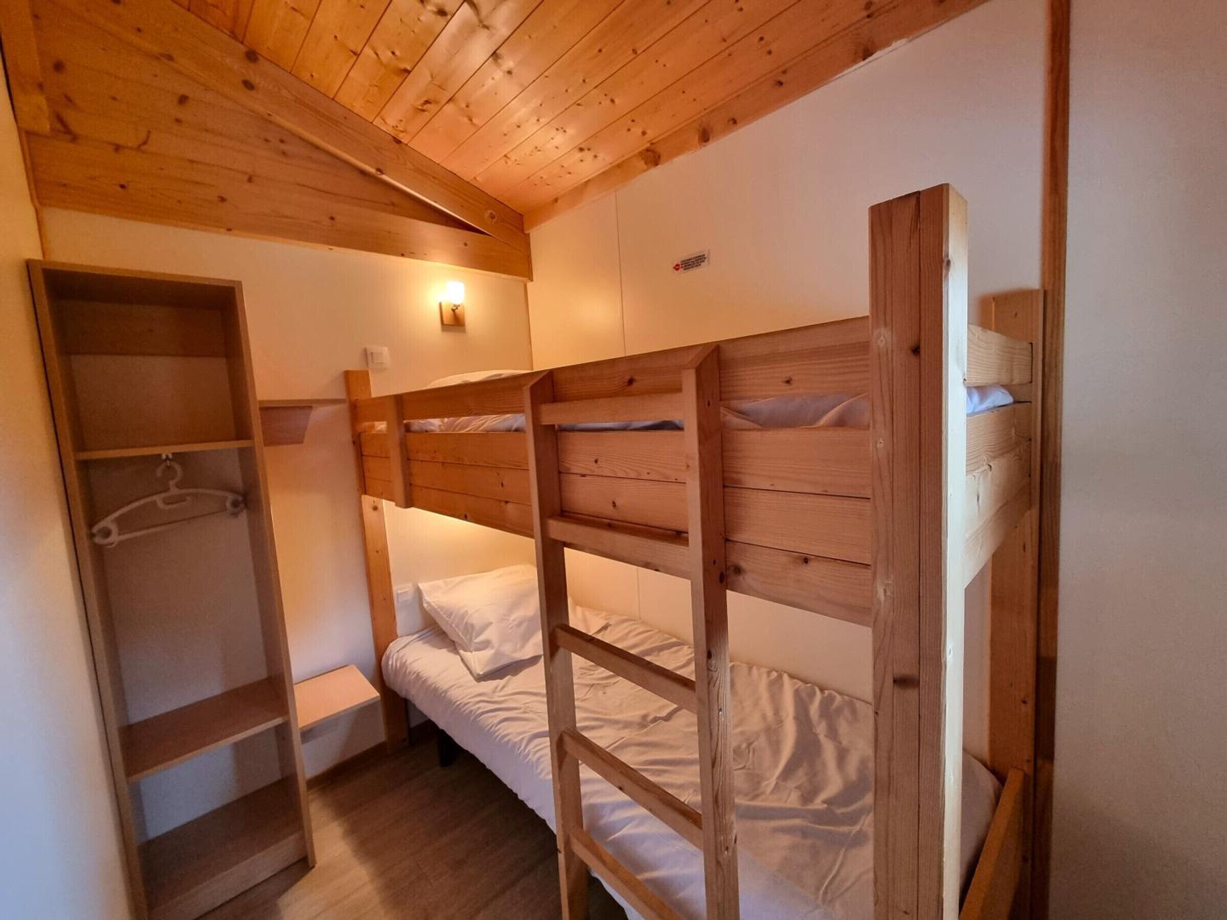 Une chambre avec un lit superposé, un plafond en bois, une armoire et une étagère.
