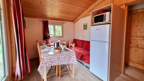 Una cabana acollidora amb interior de fusta, taula de dinar amb cadires, un sofà vermell i un refrigerador blanc.