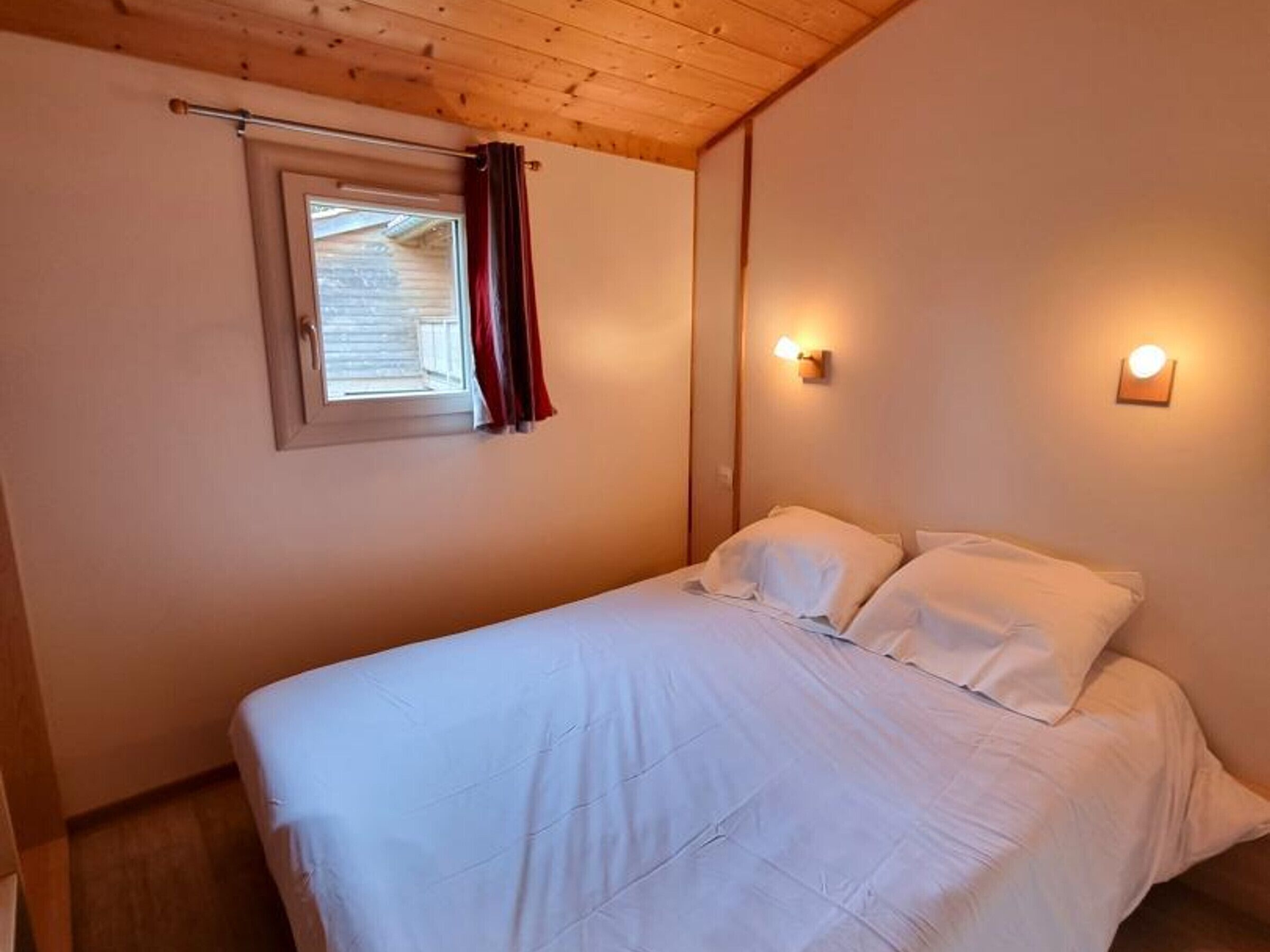 A bedroom with a single bed, a window with curtains, and wall-mounted lights.