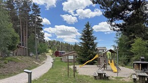 Un parc infantil amb tobogan i estructures per escalar, envoltat d'arbres i un camí de grava.