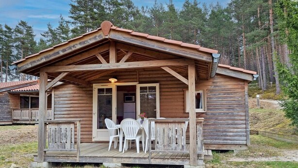 Una cabana de fusta amb un porxo, una taula amb caires i vista al bosc circumdant.