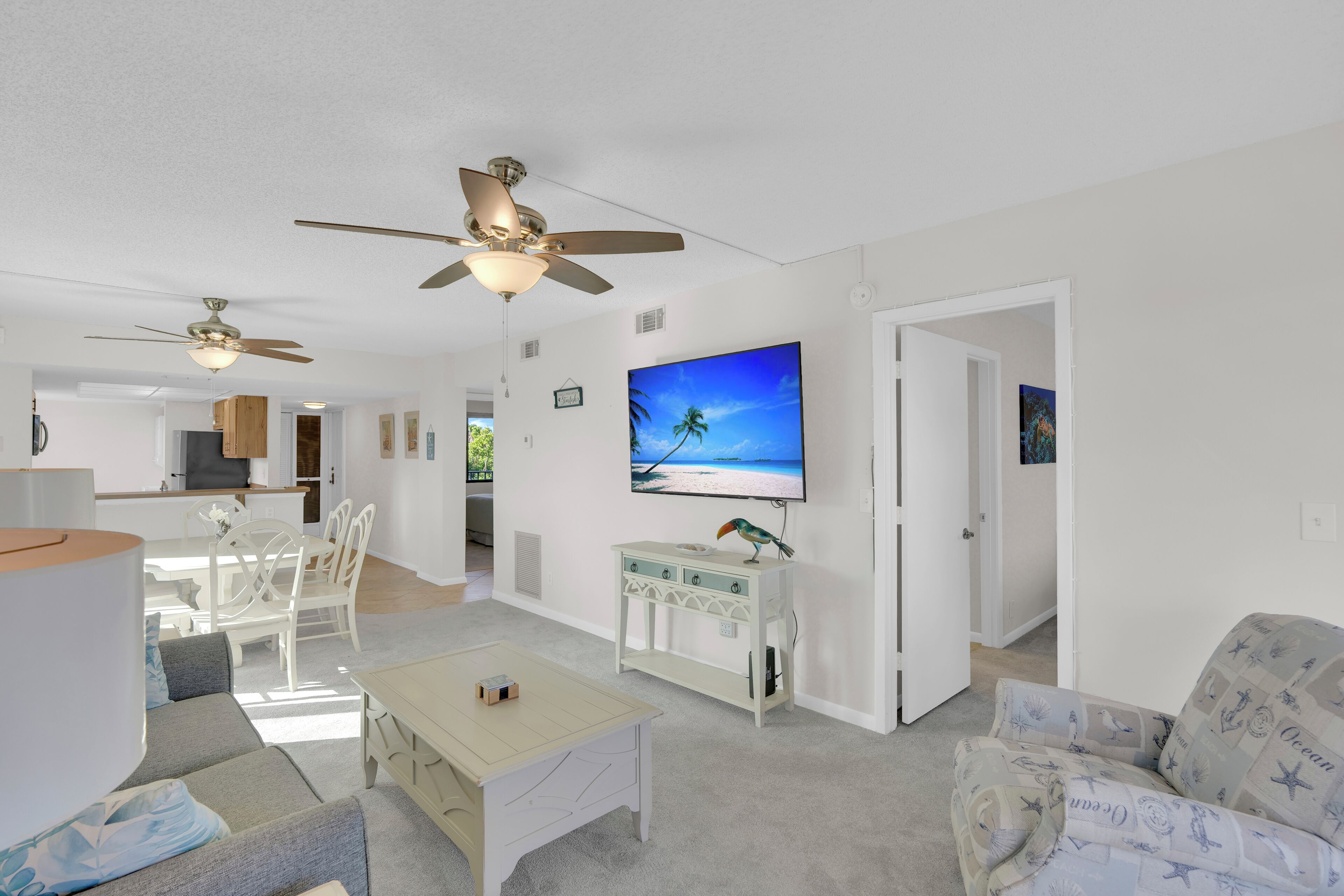 A spacious living room with a large flat-screen TV, ceiling fans, a dining area, and a cozy seating arrangement.