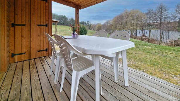 Una terraza de madera con una mesa y sillas, vista a un lago y cielo despejado.