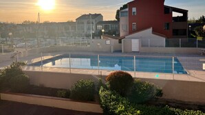 Una piscina recintata da una staccionata, immersa nel verde e affiancata da un edificio con facciata rossa.