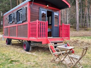 Une maison mobile rouge avec une véranda et une table entourée de chaises.