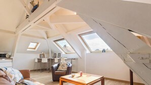A loft-style room with a sloped ceiling, skylights, a dining area with chairs, a sofa, and a coffee table. - Bright apartment, pets welcome - 2 guests (Barneville-Carteret)