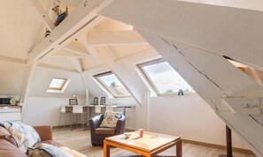 Ein Loft-Zimmer mit schrägverdachter Decke, Dachfenstern, einer Essecke mit Stühlen, einem Sofa und einem Couchtisch.
