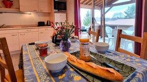 Un tavolo da pranzo con una baguette, ciotole, un vaso con fiori e una bottiglia di succo d'arancia.