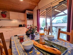 A dining table with a baguette, bowls, a vase with flowers, and a bottle of orange juice.
