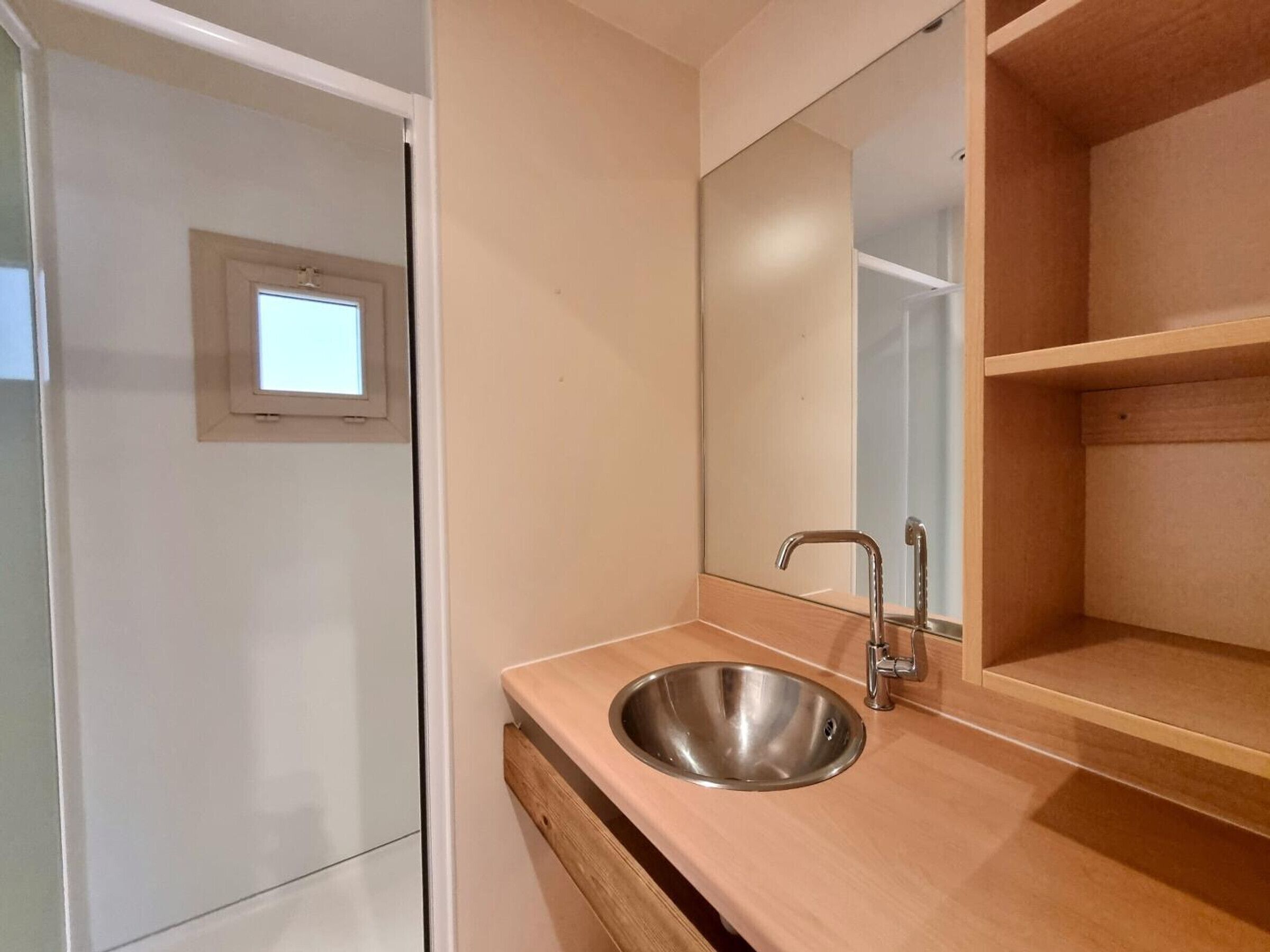 Un baño con lavamanos de acero inoxidable, espejo y tocador de madera.