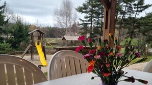 Un tavolo con un vaso viola pieno di fiori, un cartello di benvenuto e un parco giochi sullo sfondo.