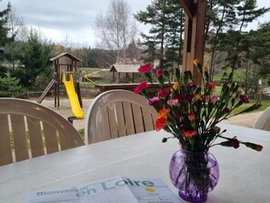 A table with a purple vase of flowers, a welcome sign, and a playground in the background.