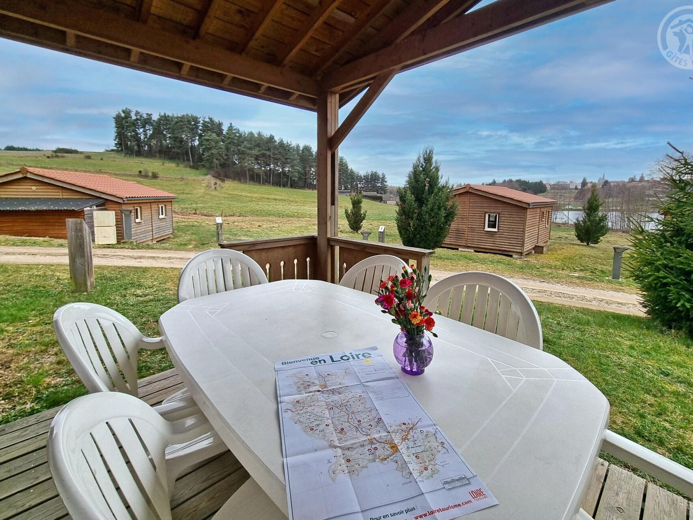 A covered outdoor area with a table, chairs, a map, and a vase with flowers.