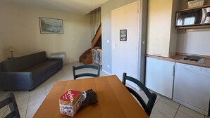 Un espai vital compacte amb taula de dinar, cadires, sofà, escala, zona de cuina i una fotografia emmarcada a la paret.