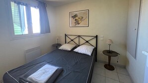 Un llit individual amb capçalera, dues taules de nit, una finestra amb cortines, un quadre penjat a la paret i un radiador.