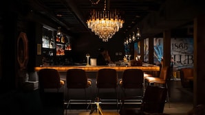 Zona de bar tenuemente iluminada con una barra central, varias sillas y un candelabro.
