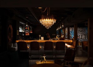 A dimly lit bar area with a central bar counter, multiple chairs, and a chandelier. - We Love You Dolly P! (Nashville)
