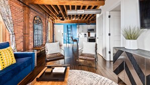 Un espacio habitable amplio con un sofá azul, dos sillas a rayas, una mesa de centro de madera y una cocina al fondo.