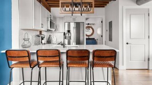 Una cocina moderna con armarios blancos, electrodomésticos de acero inoxidable y una isla central con taburetes de bar.