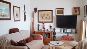 Un salon comprenant un canapé, une table basse, un téléviseur et divers tableaux encadrés accrochés au mur.