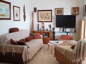 Ein Wohnzimmer mit Sofa, Couchtisch, Fernseher und verschiedenen gerahmten Bildern an der Wand.