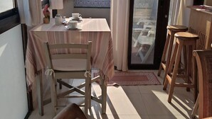 Un balcon avec une table dressée pour deux personnes, une chaise et un tabouret en bois.
