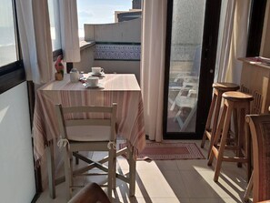 Ein Balkon mit einem Tisch für zwei Personen, einem Stuhl und einem hölzernen Hocker.