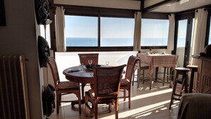 Une salle à manger baignée de lumière naturelle, avec vue sur la mer, agrémentée de tables rondes et de chaises en osier.