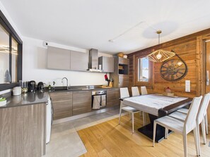 A modern kitchen with a dining area, wooden walls, and a large clock. - Les Gets - Modern Apartment for 4, Central, Wifi (Les Gets)