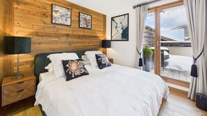 Ein Schlafzimmer mit einem hölzernen Kopfteil, einem großen Bett mit weißer Bettwäsche, zwei Nachttischen mit Lampen und Blick auf einen verschneiten Balkon.