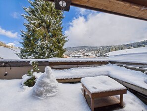 A snow-covered outdoor area with a wooden bench and a snowman, overlooking a village with houses and a mountain in the background. - Les Gets - Modern Apartment for 4, Central, Wifi (Les Gets)