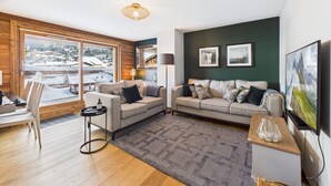 Ein modernes Wohnzimmer mit Sofa, Couchtisch, Lampe und Blick auf eine verschneite Landschaft.